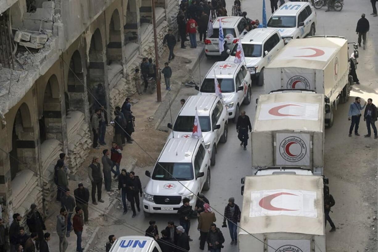 This photo released by the Syrian Red Crescent shows civilians gathering near a convoy of vehicles of the Syrian Red Crescent in Douma, eastern Ghouta, a suburb of Damascus, Syria, on Monday. Desperate for food and medicine, Syrian civilians in the war-ravaged eastern suburbs of Damascus hoped for relief Monday as a 46-truck aid convoy began entering the rebel stronghold, the first such shipment in months.