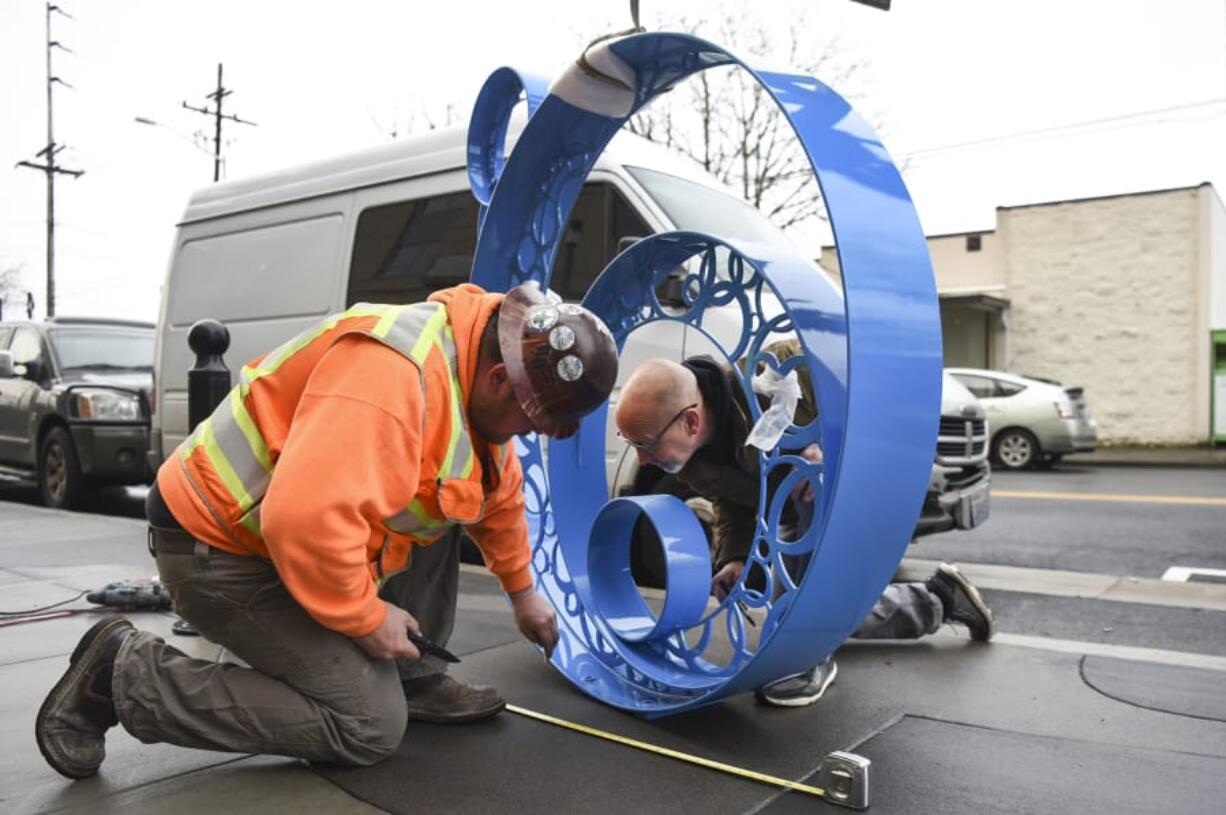 Jamason Lindeman of Robertson and Olson, left, and Dave Frei, a local artist, determine the correct spot for a sculpture titled “Bubbles” that Frei and his wife, Jennifer Corio, created outside The Uptown Apartments along Washington Street in Vancouver.