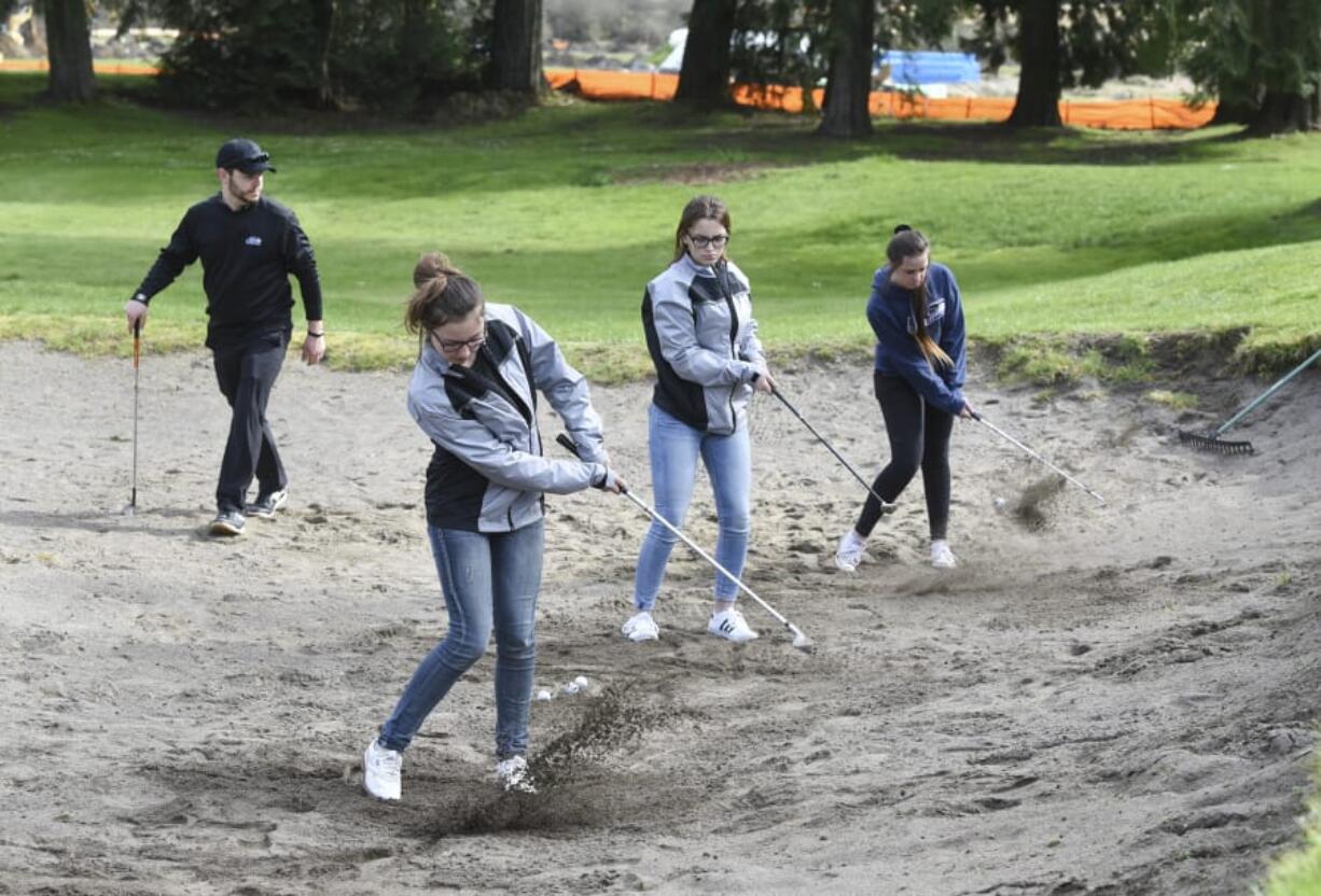 Coach Joe Cain, left, watches at Battle Ground High School golfers Grace Ritola, Jessica Spalding and Reilly Joma practice at The Cedars on Salmon Creek. The course sold 30 acres to a real estate developer last year in the hopes of landing more neighbors and business.