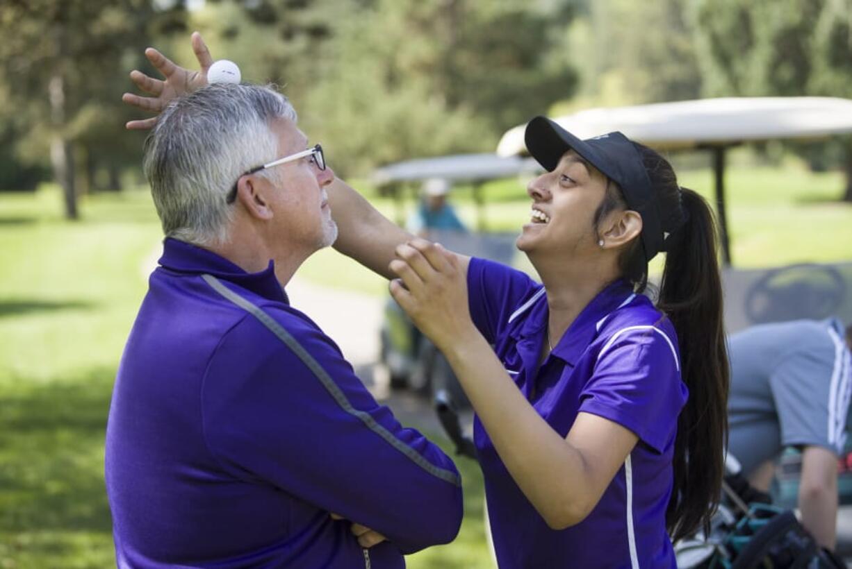 Heritage sophomore Shweta Nand, right, balances a golf ball on her coaches head, Dwight Patterson, in-between holes at the Prairie Invitational at Lewis River Golf Course in Woodland, Wednesday April 25, 2018.