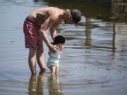 Michael Gile of Vancouver, left, and Hannah Forslund, not pictured, play with their daughter Lily, 1, right, at the edge of Klineline Pond in Vancouver on April 25.