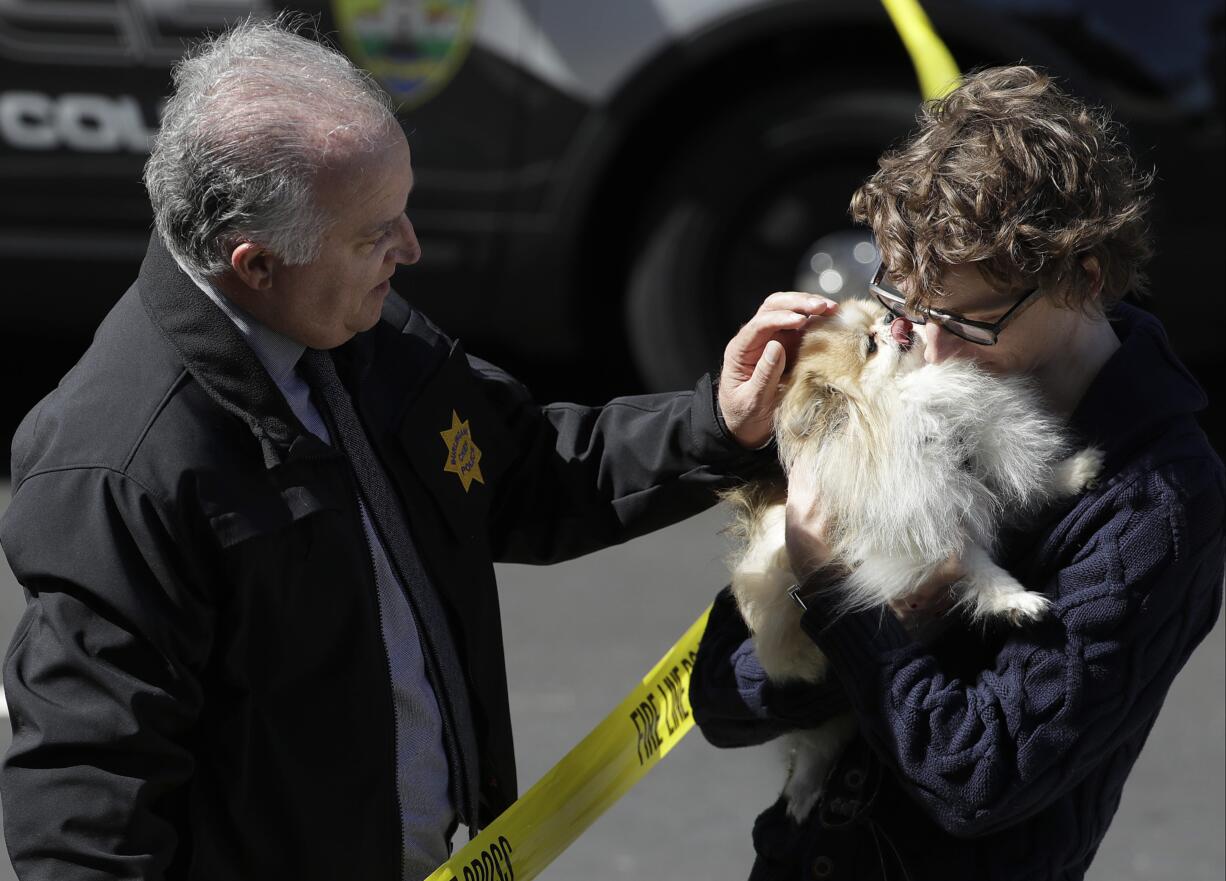 Burlingame Chief of Police Eric Wollman, left, hands a dog named Kimba to a man who wished to remain unidentified but said he worked for YouTube, outside the company's headquarters, in San Bruno, Calif., Tuesday, April 3, 2018. A woman opened fire at YouTube headquarters Tuesday, setting off a panic among employees and wounding several people before fatally shooting herself, police and witnesses said.