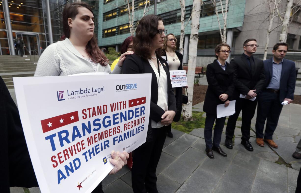 FILE - In this March 27, 2018, file photo, plaintiffs Cathrine Schmid, second left, and Conner Callahan, second right, listens with supporters during a news conference in front of a federal courthouse following a hearing in Seattle. A federal judge in Seattle has ordered President Donald Trump not to take any action barring transgender troops from serving in the military, finding that it's unclear whether recent tweaks to his administration's policy are constitutional. In an order Friday, April 13, 2018, U.S. District Judge Marsha Pechman said that because the tweaks were announced just last month, the parties had not had time to argue about whether the policy is unconstitutionally discriminatory or whether the military is entitled to deference.