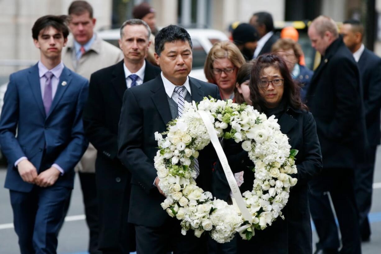 The father of Lingzi Lu, Jun Lu, foreground left, and her aunt Helen Zhao, foreground right, carry a wreath ahead of the family of Martin Richard, background from left, Henry, Bill, Denise and Jane, partially hidden, during a ceremony at the site where Martin Richard and Lingzi Lu were killed in the second explosion at the 2013 Boston Marathon, Sunday, April 15, 2018, in Boston.