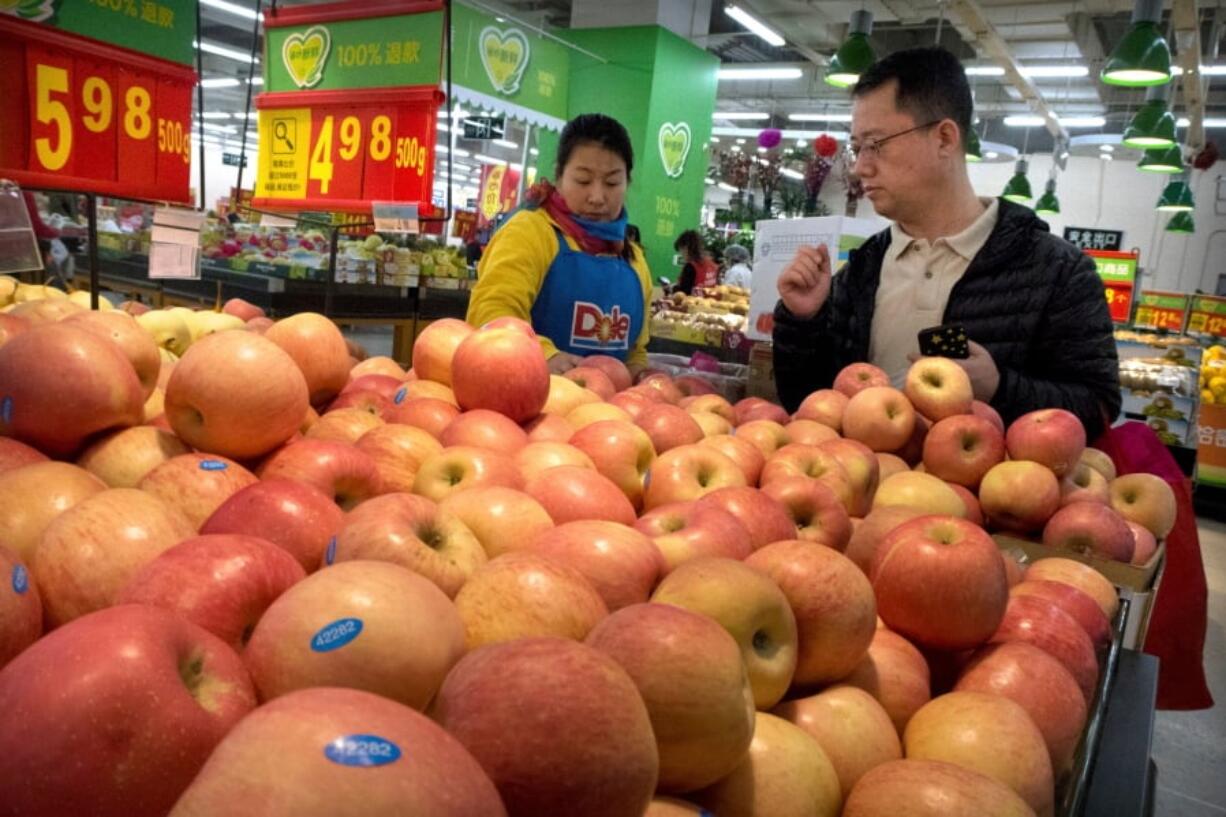 A woman wearing a uniform with the logo of Dole, an American produce company, helps a customer shop for apples at a supermarket in Beijing.