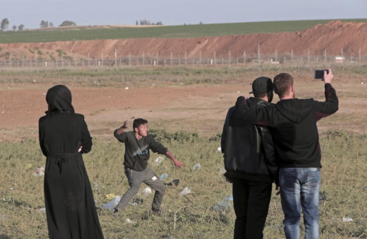 A Palestinian uses his phone to take photos while a protester slings stones towards Israeli soldiers on the other side of the fence during clashes with Israeli troops along the Gaza Strip border with Israel, east of Beit Lahiya, Gaza Strip. The Israeli military’s open-fire policies came under more scrutiny as two amateur videos emerged purportedly showing two Palestinians being shot — one killed and one wounded — while not posing any apparent threat to soldiers. The Israeli military accused Hamas on Sunday of releasing videos that were incomplete, edited or “completely fabricated,” but did not elaborate.