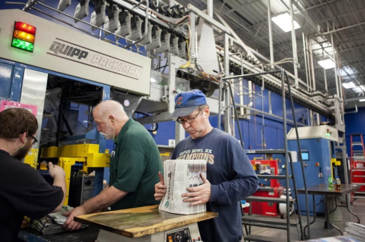 In this April 11, 2018, photo, production handler Pat Breidenbach straightens out a stack of newspapers while working at the Janesville Gazette Printing & Distribution plant in Janesville, Wis. Newspaper publishers across the U.S. already strapped by years of declining revenue say they’re dealing with an existential threat: Recently imposed tariffs on Canadian newsprint driving up their business costs.