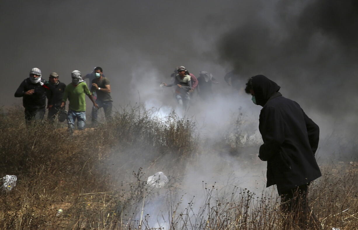 Palestinian protesters run to cover from teargas fired by Israeli troops after they burn tires near the fence during a protest Friday at the Gaza Strip’s border with Israel, east of Khan Younis.