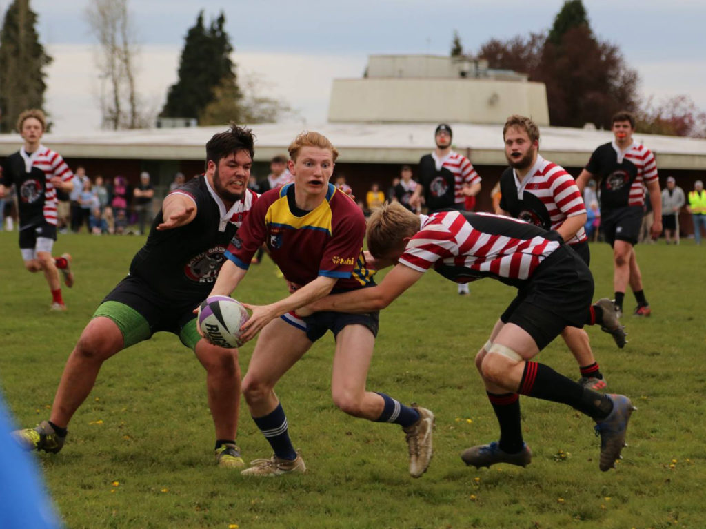 Prairie's Payton Millet passes the rugby ball while Battle Ground's Adam Lingle (left) and Aiden Wheeler look to make the tackle.