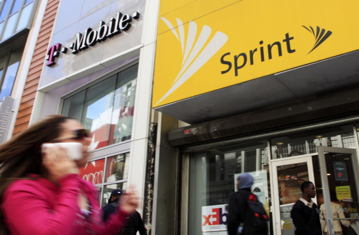 FILE- In this April 27, 2010 file photo, a woman using a cell phone walks past T-Mobile and Sprint stores in New York. T-Mobile and Sprint are trying again to combine in a deal that would reshape the U.S.