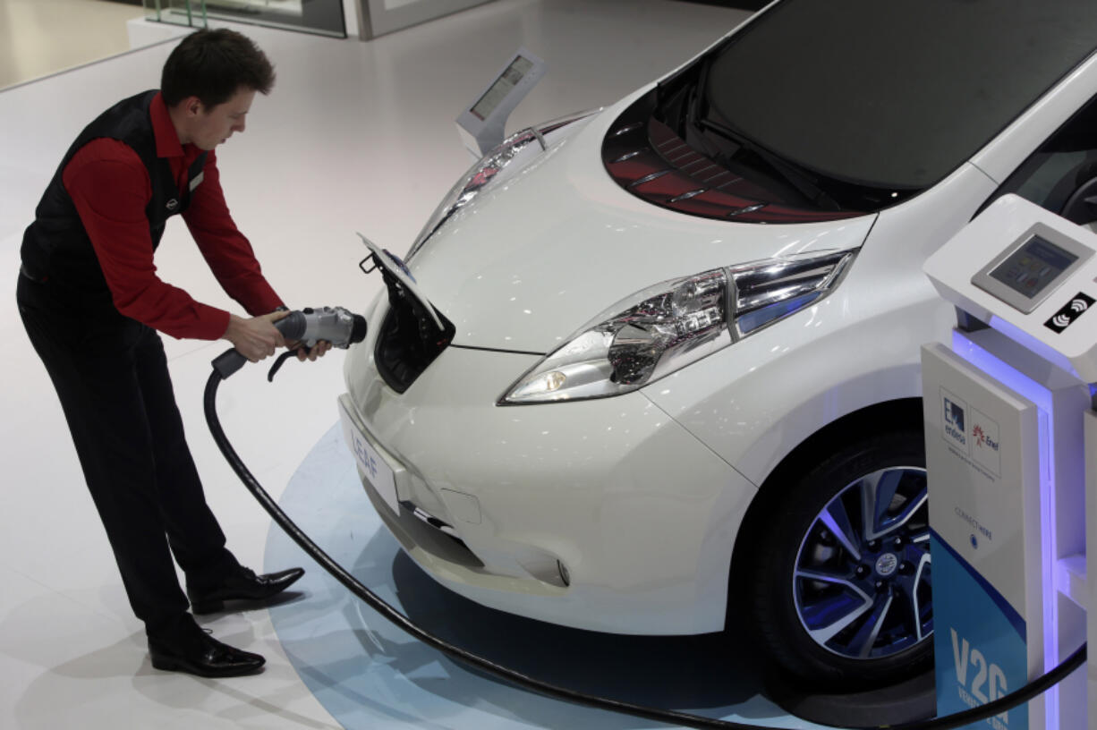 An employee prepares to install a charging plug in the socket of a Nissan Leaf electric automobile at the 85th Geneva International Motor Show in Geneva, Switzerland, on March 4, 2015.