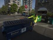 Ryan Mayer of Waste Connections of Washington empties a garbage bin at the corner of West Ninth and Washington streets. A task force of city officials and business owners is proposing new dumpster enclosures and fines to corral garbage.