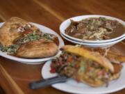 A calzone with meatballs, mozzarella and basil, left, is served with the Brewer’s poutine with shredded pork, top right, and the Peloton steak sandwich at Hopworks Urban Brewery.