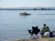 A boat cruises on the Columbia River as a beachgoer relaxes earlier this year at Wintler Park. Warmer weather means more people are on the water, which compounds the many dangers — especially when snowmelt means streamflows are high and water temperatures low.