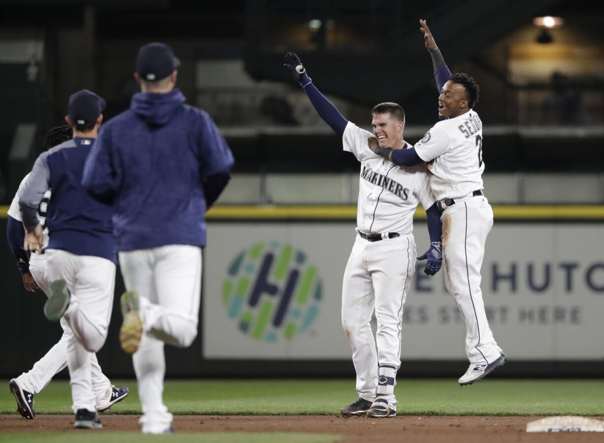 Seattle Mariners players rush onto the field to greet Ryon Healy, second right, as Jean Segura jumps on him after Healy's game winning, 1-run single against the Los Angeles Angels in the 11th inning of a baseball game Saturday, May 5, 2018, in Seattle. The Mariners won 9-8.