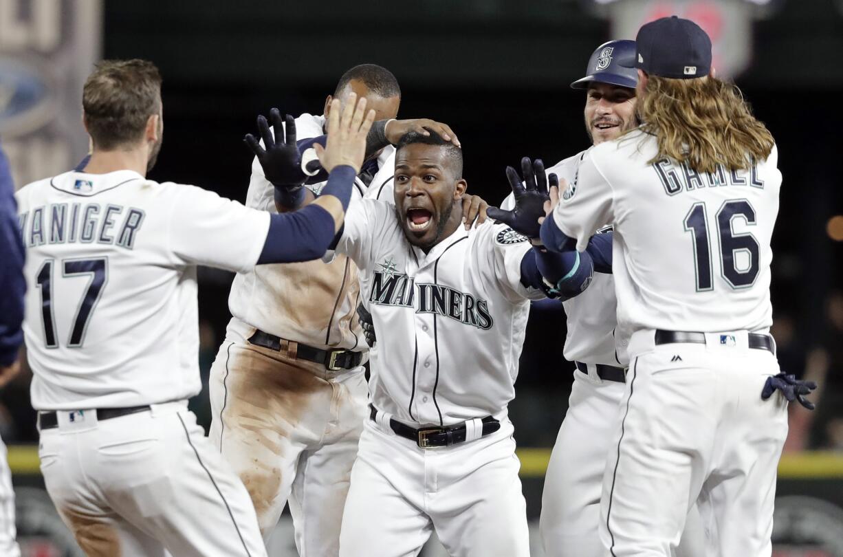 Seattle Mariners' Guillermo Heredia, center, is cheered by teammates after hitting a one-run single to beat the Texas Rangers in the 11th inning of a baseball game Tuesday, May 15, 2018, in Seattle. The Mariners won 9-8.