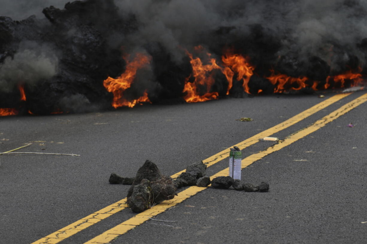 Lava burns across a road Saturday as an offering to the volcano goddess lies in the foreground in the Leilani Estates subdivision near Pahoa, Hawaii. Glowing plumes of lava have shot hundreds of feet into the air at points, officials said, and black-and-orange ribbons of rock have curled into roadways.