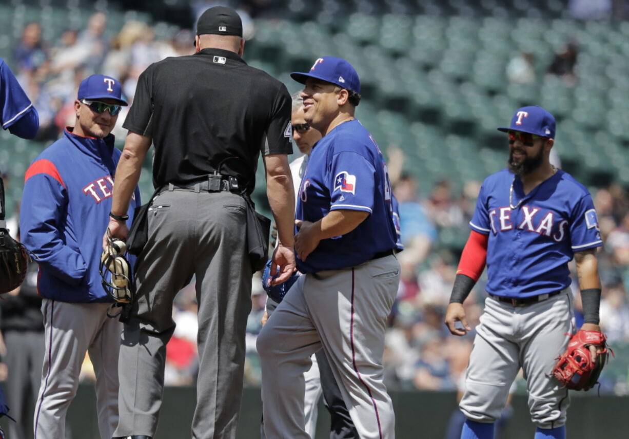 Texas Rangers starting pitcher Bartolo Colon, second from right, smiles as he returns to the mound after talking with a Rangers’ trainer after Colon was hit by a ball hit by Seattle Mariners shortstop Jean Segura during the fourth inning of a baseball game, Wednesday, May 16, 2018, in Seattle. (AP Photo/Ted S.