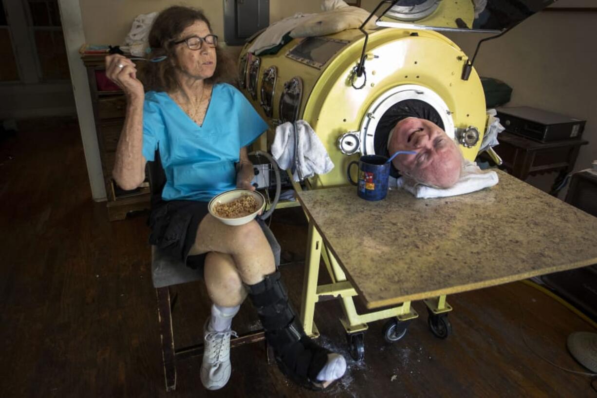 Paul Alexander chats with caregiver Kathryn Gaines as he drinks coffee and she eats breakfast beside his iron lung at his home in Dallas on April 27. Alexander is one of the few people left who uses an iron lung to help facilitate breathing for those affected by polio. Smiley N.