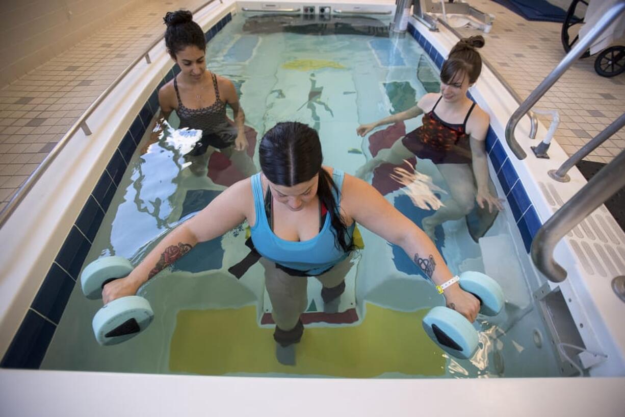 Catherine Martinez of Vancouver, foreground, who mysteriously lost the ability to walk on her birthday in May, practices leg-strengthening exercises with student physical therapist Sabrita Cohen, background left, and physical therapist Jane Gyarmaty at PeaceHealth Southwest Medical Center. Martinez is pictured wearing four-pound weights on each leg as she practices walking up a step in the therapy pool. Martinez has been in the hospital nearly a month, and doctors still don’t know the root cause of Martinez’s ailment.