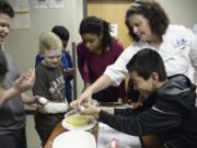 Alison Dolder, department head for professional baking and pastry arts at Clark College, right, helps sixth-grader Eduardo Castellon, right, crack an egg while Eduardo Santos, left, Jaden Cleere and Janoah Stegall watch nearby during a baking lesson at the Boys & Girls Clubs of Southwest Washington in April 2017.