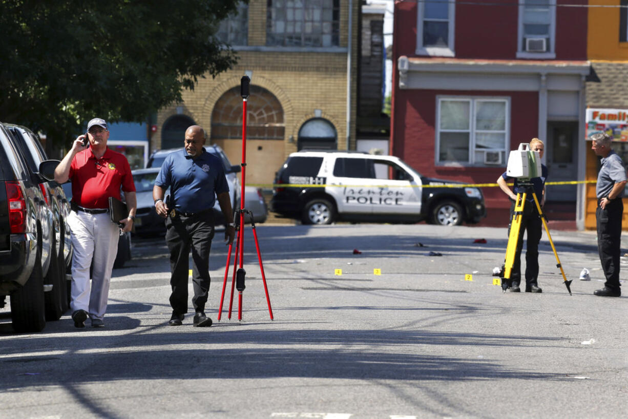 Mercer County Prosecutor Angelo Onofri, left, walks past investigators standing in a street near evidence markers outside the warehouse building where the Art All Night Trenton 2018 festival that was the scene of a shooting that resulted in numerous injuries and at least one death Sunday, June 17, 2018, in Trenton, N.J.