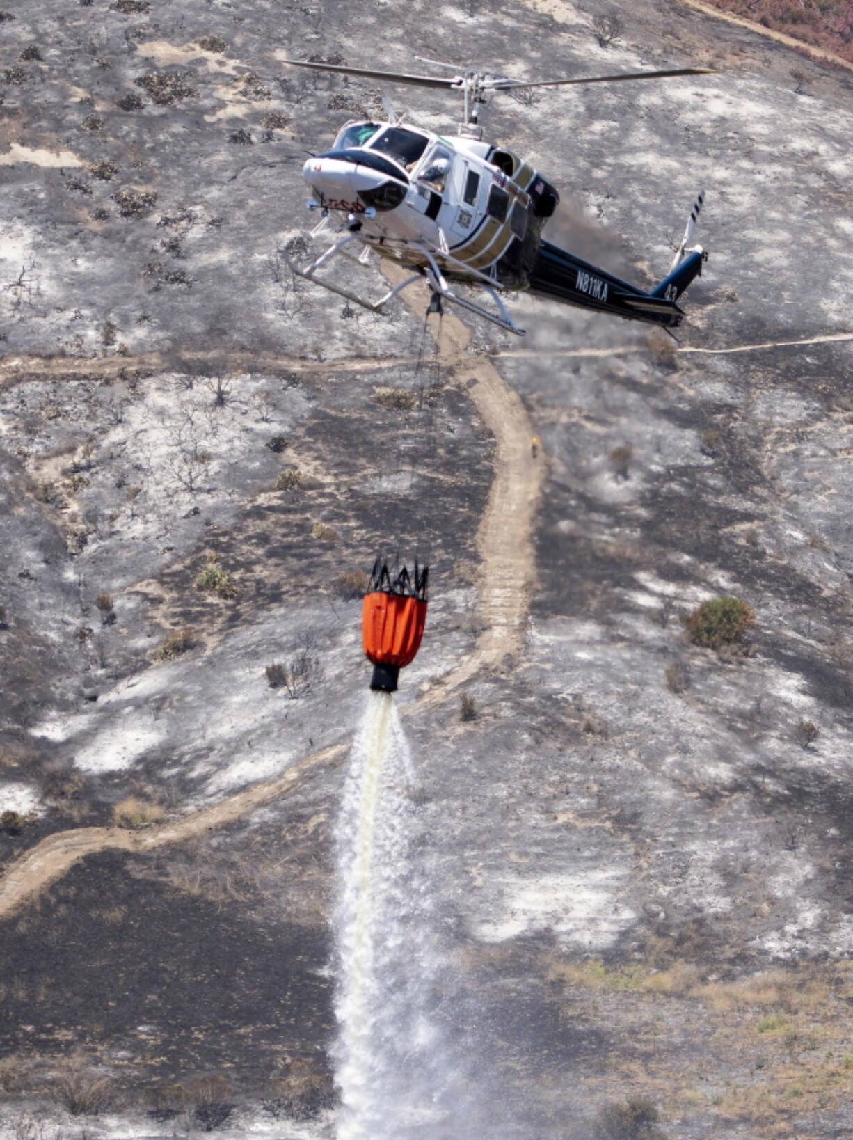 A helicopter from the Fresno County Fire Department makes a water drop on the remnants of a brush fire in Wood Canyon in the hills below Soka University in Aliso Viejo, Calif., on Sunday. The Orange County Fire Authority said Sunday that the 150-acre blaze is 10 percent contained after churning through thick underbrush that hasn’t burned in years.