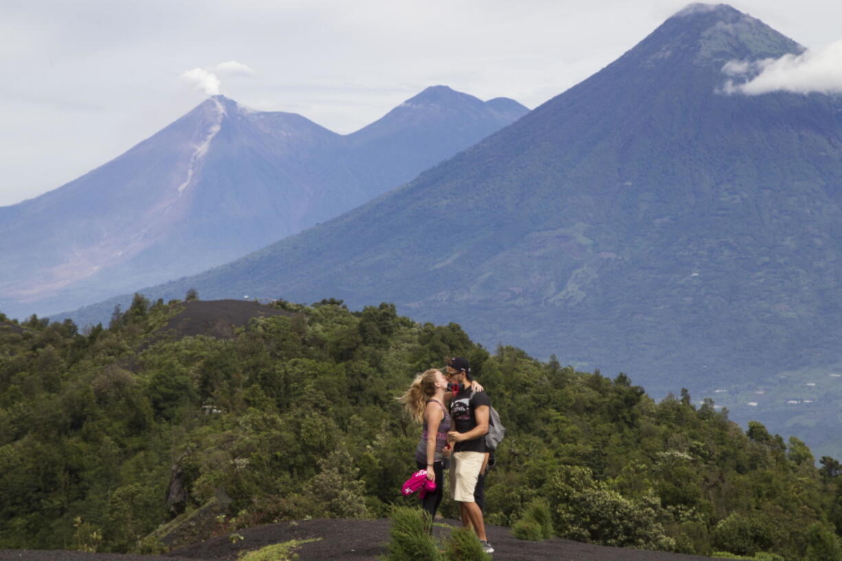 A couple of tourists kiss with the view of the volcanoes, Fuego, left, Acatenango, center, and Agua, right, in the background, from a point in the climb to the Pacaya Volcano, in San Francisco de Sales, Guatemala. Volcano tourism is the life blood of villages like San Francisco de Sales, perched near Pacaya’s peak, and for locals it is a question of learning to live with a generous monster.