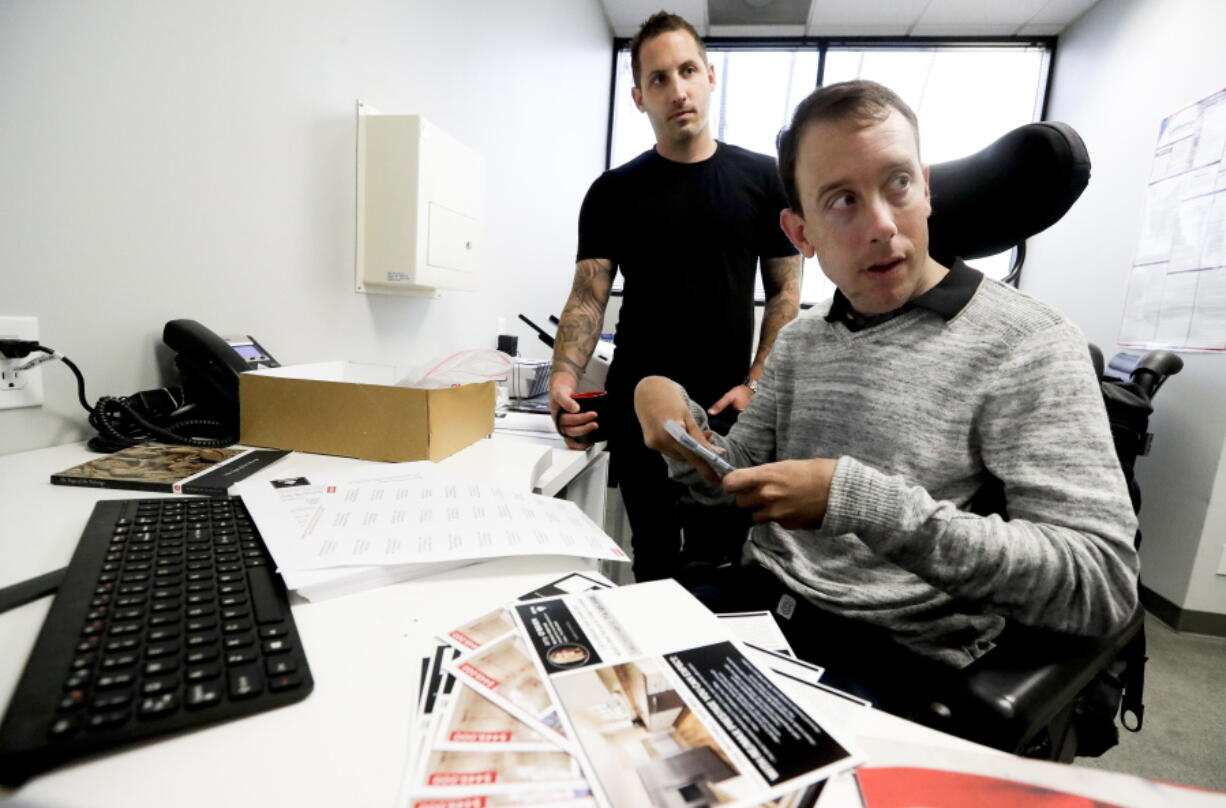 Miles Thornback, right, who has cerebral palsy, works on marketing campaigns for agents with owner Jay O’Brien at RE/MAX Prestige real estate office in Costa Mesa, Calif.