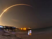 A SpaceX Falcon 9 rocket lifts off from Cape Canaveral Air Force Station with the SES-12 commercial communications satellite in Cape Canaveral, Fla., on Monday. The rocket launched at 12:45 a.m. Monday morning with a satellite bound for geostationary orbit. A long exposure with a wide angle lens of the launch shows the rocket rising over the Cocoa Beach Pier in the foreground, and the waning gibbous moon rising in the east.