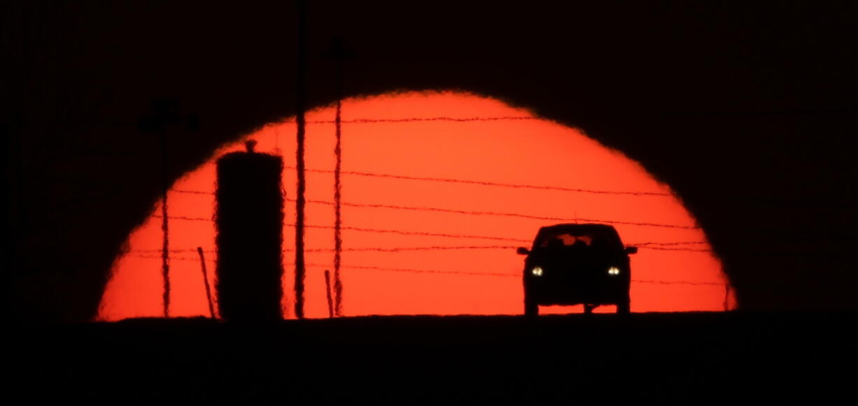 A car is silhouetted against the setting sun as it travels along Interstate 70 in Kansas City, Kan., on March 27, 2013. Suddenly road trips are trendy again. Surveys from MMGY, Ford and AAA show their popularity is up.