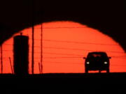 A car is silhouetted against the setting sun as it travels along Interstate 70 in Kansas City, Kan., on March 27, 2013. Suddenly road trips are trendy again. Surveys from MMGY, Ford and AAA show their popularity is up.