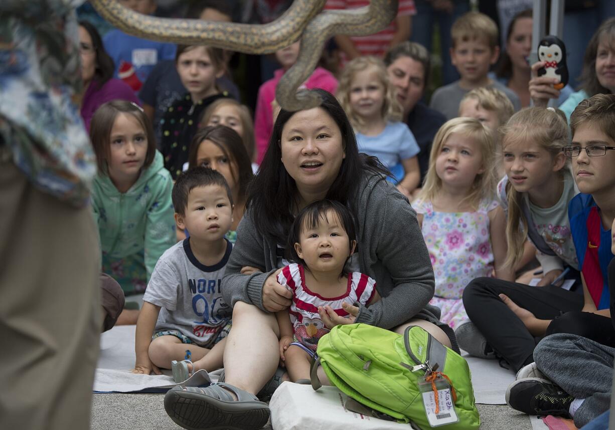 Young Zhang, 3, front row from left, his mom, Megan Chan, and his sister, Xia Zhang, 2, get a front row seat to view an anaconda while joining a crowd of reptile fans during a presentation by The Oregon Reptile Man, Richard Ritchey, at Three Creeks Community Library on Thursday morning, July 19, 2018. The event was part of the library's summer reading program.