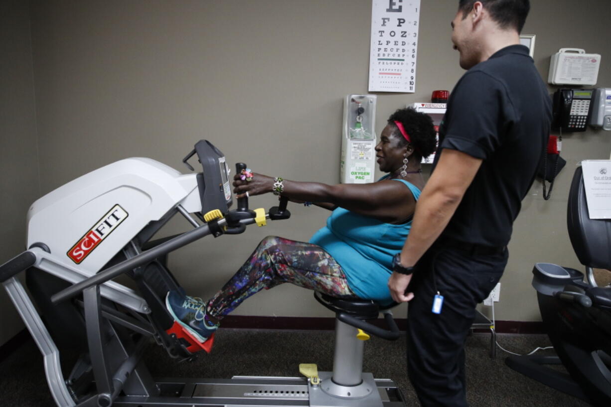 In a Monday, July 16, 2018 photo, Virta Woodard, a 56-year-old diabetic, chats with wellness coach Ryan Manuwa while exercising at Nifty After Fifty fitness centers in Lakewood, Calif. Woodard gets weekly phone calls from her care manager, and she’s started hitting Nifty After Fifty fitness centers since she signed up for a program called “Togetherness” covered by the Blue Cross-Blue Shield insurer Anthem Inc. The health care system is becoming more focused on keeping patients healthy instead of waiting to treat them once they become sick or wind up in the hospital. The 56-year-old diabetic lives with daily pain due to her disease and a injuries from a car accident, but she’s lost 34 pounds since joining the program. (AP Photo/Jae C.