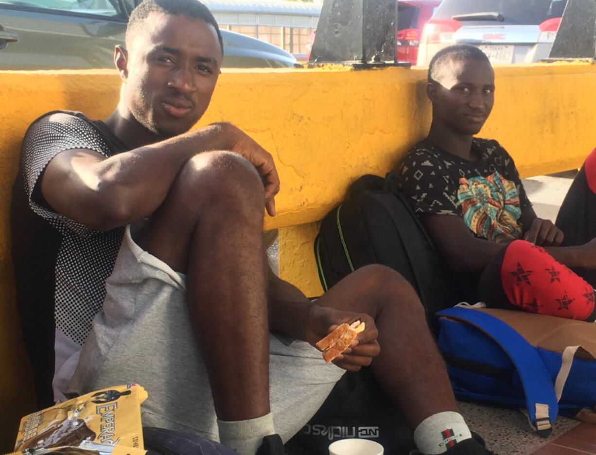 Mamadou Aliou Barry, left, departed from his native Guinea in West Africa when he was 14, a few years ago, waits for entry to the U.S. on the Gateway Bridge in Matamoros, Mexico, which connects to Brownsville, Texas. He said as part of the minority ethnic Fula group, he fears for his life and carries prints of a picture of him and a friend together and a picture of his friend after he was murdered, for his asylum interview.