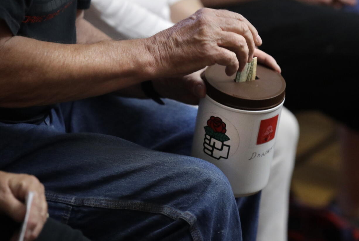 A patron puts a bill in a donation bucket, which features a red rose symbol, during a meeting of members of the Southern Maine Democratic Socialists of America in Portland, Maine, Monday, July 16, 2018. On the ground in dozens of states, there is new evidence that democratic socialism is taking hold as a significant force in Democratic politics. The red rose is a symbol of democratic socialism.