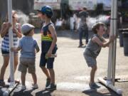 Lilly Drew, 6, from left, Lukas King, 6, Andi King, 4, and Oliver Drew, 3, all of Portland, cool down by drinking water from a misting station at the Clark County Fair on Tuesday afternoon.