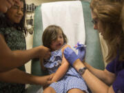 Abigail Crumrine, 4, gets an injection from Kris Black, right, on Wednesday at the Free Clinic of Southwest Washington. Abigail gets support from her sister, Mary, second from left.