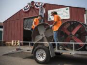 Connor Flolo, left, and Wyatt Samson, both 17 and of Camas, pick up fans Monday morning from the animal barns at the Clark County Fairgrounds in Ridgefield. About 70 fans were divided between the barns to help keep animals cool during a heat wave that lasted through most of the fair.