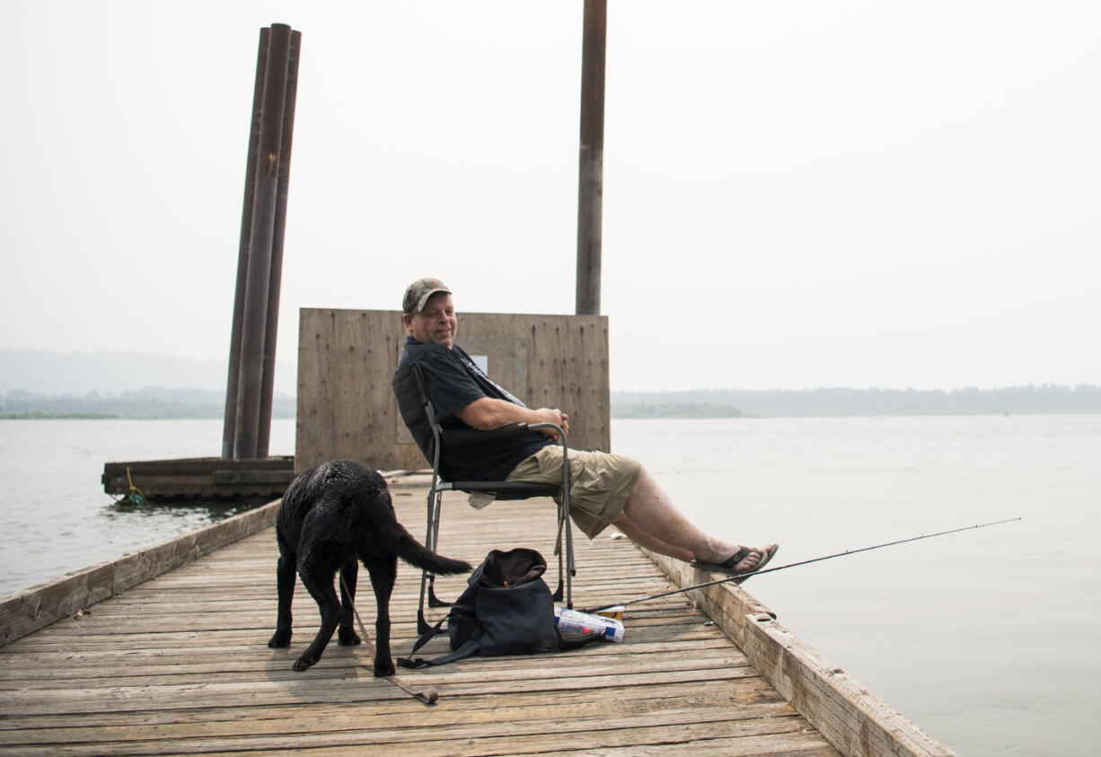 Randy Rolene of Vancouver relaxes with his dog Bella and fishes off of the dock at Steamboat Landing Park in Washougal on Tuesday, Aug. 14, 2018. Rolene said he decided to come out to the river to take his dog for a swim, but he'll probably head home early because of the smoke. "It's nasty," he said.