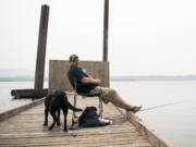 Randy Rolene of Vancouver relaxes with his dog Bella and fishes off of the dock at Steamboat Landing Park in Washougal on Tuesday, Aug. 14, 2018. Rolene said he decided to come out to the river to take his dog for a swim, but he'll probably head home early because of the smoke. "It's nasty," he said.