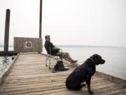 Randy Rolene of Vancouver relaxes with his dog Bella and fishes off of the dock at Steamboat Landing Park in Washougal on Tuesday, Aug. 14, 2018. Rolene said he decided to come out to the river to take his dog for a swim, but he'll probably head home early because of the smoke. "It's nasty," he said.