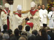 FILE – In this Oct. 1, 2012, file photo, the Most Rev. Donald Trautman, second from left, retiring bishop of Erie, Pa., prays and lays his hands on the head of Monsignor Lawrence T. Persico, kneeling, the bishop-elect of Erie, Pa., during Persico's rite of ordination at St. Peter Cathedral in Erie, Pa. The Most Rev. Charles J. Chaput, left, archbishop of Philadelphia, served as principal consecrator during the service, and the Most Rev. Lawrence E. Brandt, center, bishop of Greensburg, Pa., served as co-consecrator with Trautman. A grand jury report released Tuesday, Aug. 14, 2018, documenting seven decades of child sexual abuse by Roman Catholic priests in Pennsylvania says Trautman allowed priests to continue restricted or regular duties despite credible allegations of abuse, was dishonest to the public or other officials about the diocese's knowledge of abuse and reassigned priests with credible accusations to keep them in the ministry. Trautman and his lawyer deny the bishop ever covered up sexual abuse by priests.