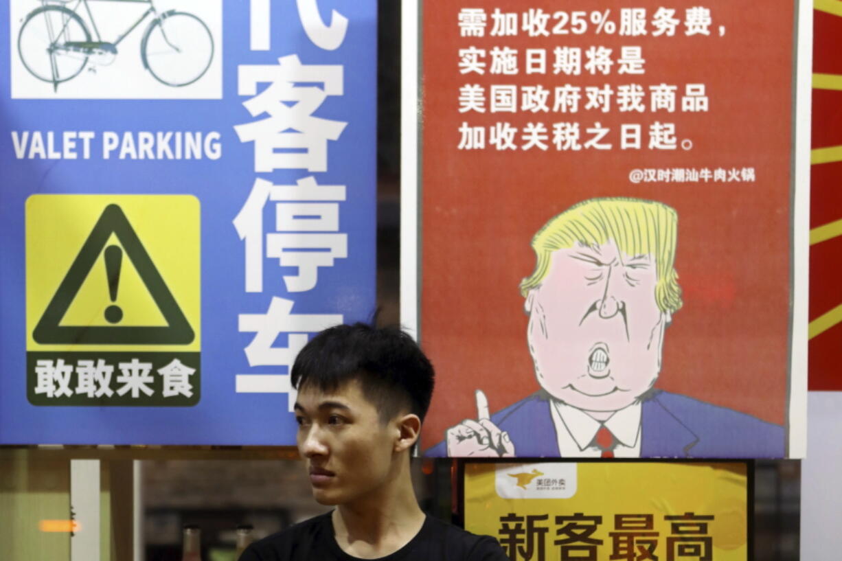 A man sits in front of a billboard stating that American customers will be charged 25% extra due to ongoing China-U.S. trade tensions at a restaurant in Guangzhou in southern China’s Guangdong Province. The United States and China imposed more tariff hikes on billions of dollars of each other’s automobiles, factory machinery and other goods Thursday, Aug. 23, 2018, in an escalation of a battle over Beijing’s technology policy that companies worry will chill global economic growth.