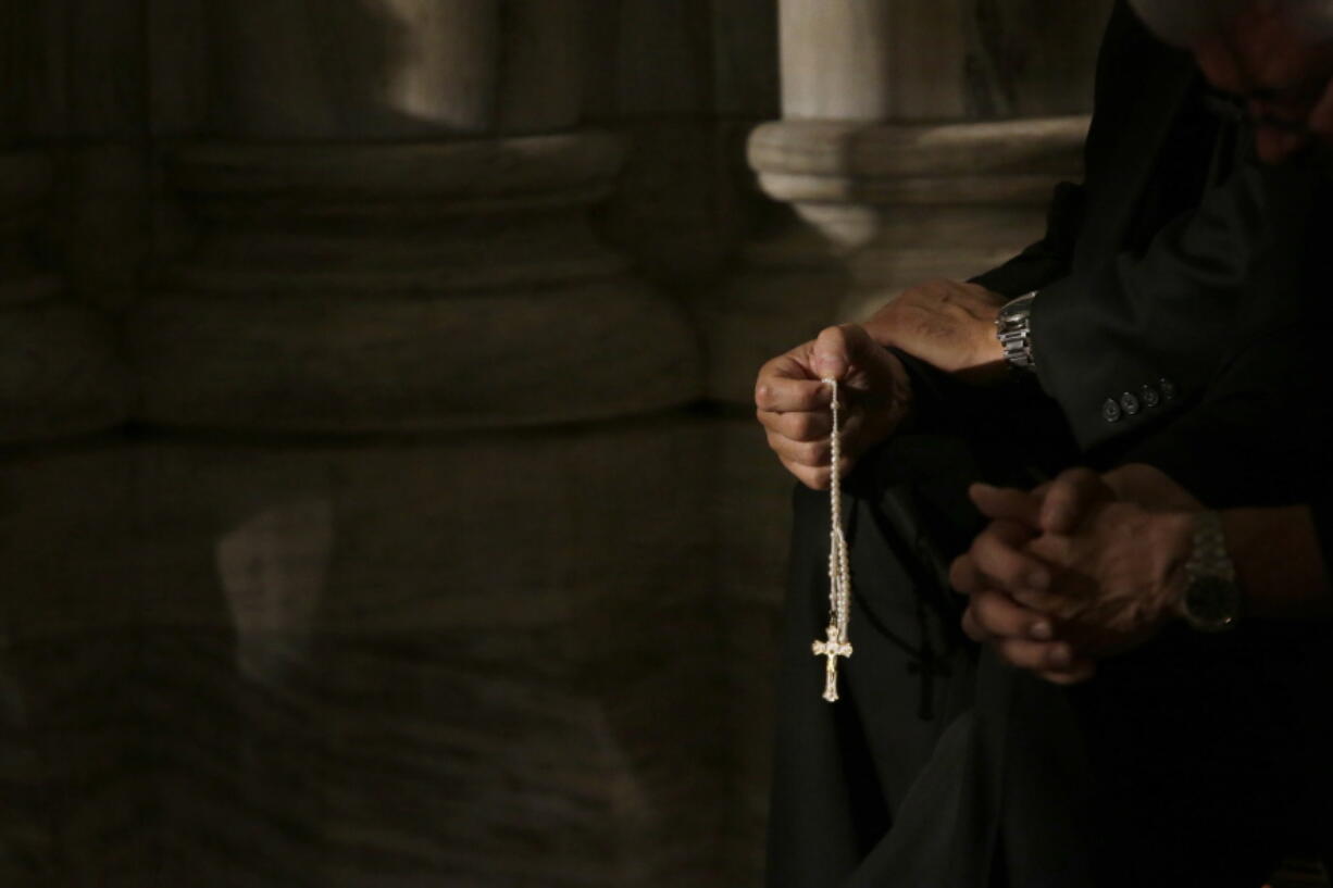 FILE- In this Sept. 24, 2015, file photo a member of the clergy prays the rosary as he waits for Pope Francis to arrive at St. Patrick’s Cathedral for evening prayer service in New York. Across the U.S., Catholics once faithful with their financial support to their churches are searching for ways to respond to the constant sex-abuse scandals that have tarnished the institution in which they believe, with back-to-back scandals in the past two months.