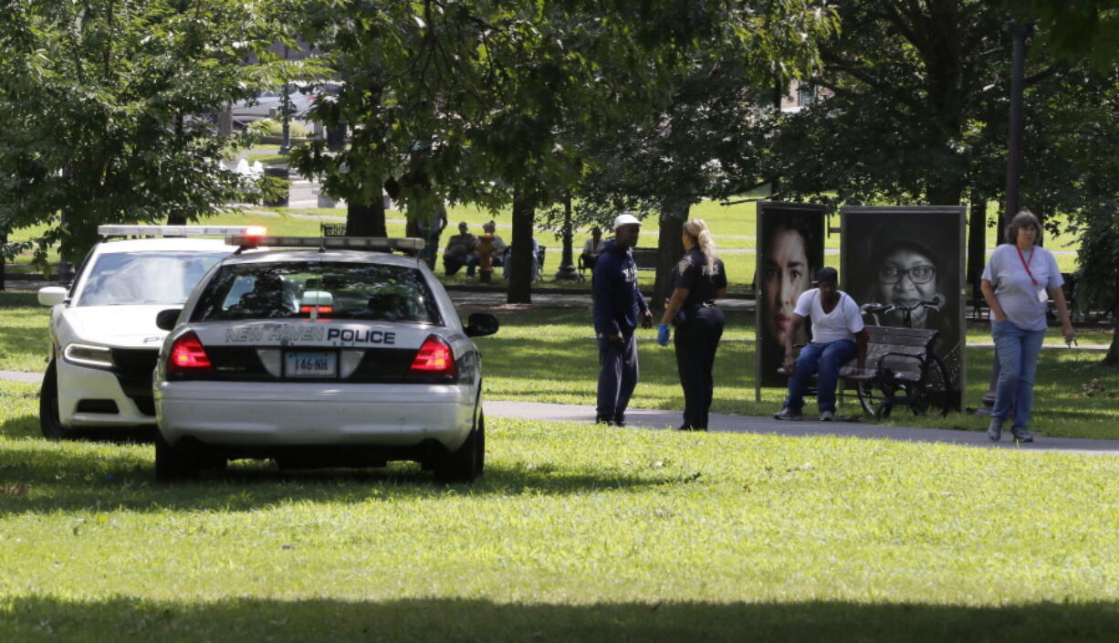 A police officer speaks to a man walking on New Haven Green, Wednesday, Aug. 15, 2018, in New Haven, Conn. A city official said more than a dozen people fell ill from suspected drug overdoses on the green and were taken to local hospitals.