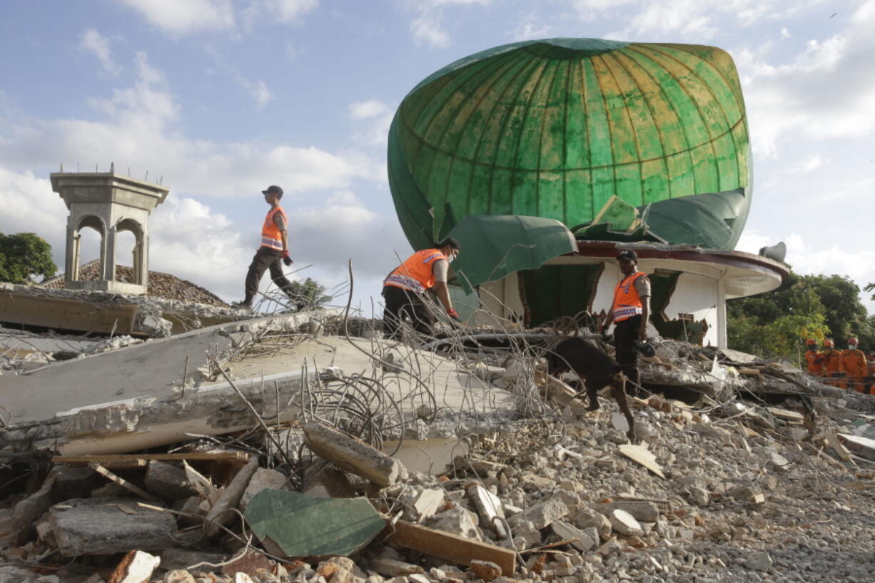 Rescuers with a sniffer dog search for victims in the rubble of a mosque Tuesday in North Lombok, Indonesia.