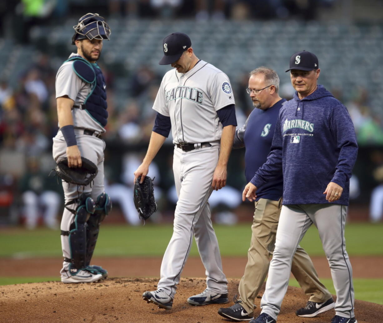 Seattle Mariners pitcher James Paxton, second from left, is escorted off the field after being hit by a ball in the first inning of a baseball game against the Oakland Athletics Tuesday, Aug. 14, 2018, in Oakland, Calif.