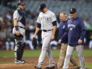 Seattle Mariners pitcher James Paxton, second from left, is escorted off the field after being hit by a ball in the first inning of a baseball game against the Oakland Athletics Tuesday, Aug. 14, 2018, in Oakland, Calif.