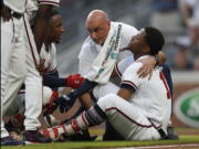 Atlanta Braves’ Ronald Acuna Jr. (13) is tended to by a member of the training staff as Ozzie Albies talks to him after Acuna was hit by a pitch from Miami Marlins starting pitcher Jose Urena during the first inning of a baseball game Wednesday, Aug. 15, 2018, in Atlanta.